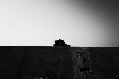 Low angle view of silhouette man sitting against clear sky