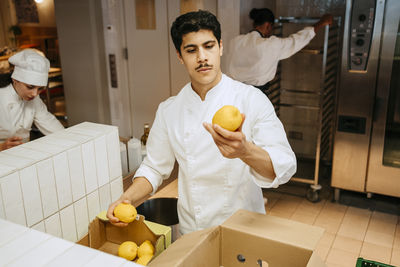 Male chef checking quality of lemon while standing in commercial kitchen