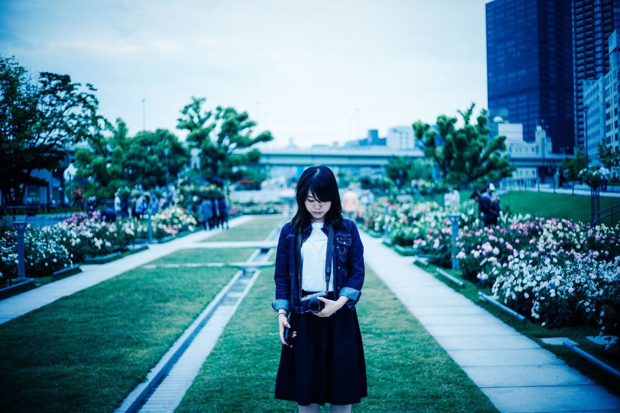 lifestyles, young adult, casual clothing, person, leisure activity, full length, young women, building exterior, standing, portrait, looking at camera, front view, built structure, smiling, architecture, tree, street, city