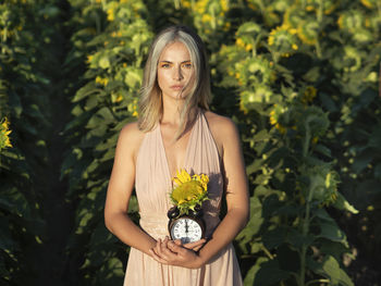 Portrait of young woman with clock in field of sunflowers