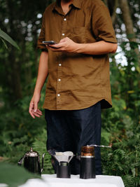 Midsection of man holding mobile phone while standing in yard