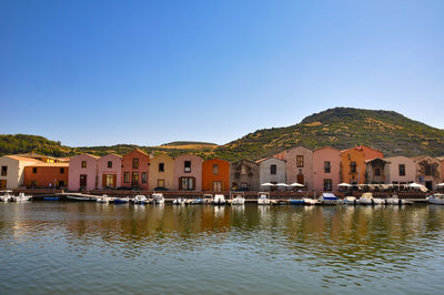 Houses by river and buildings against clear blue sky