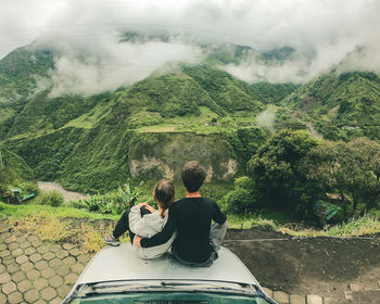 Rear view of couple looking at mountain while sitting on car