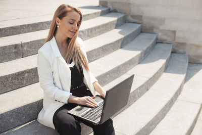 Young woman using mobile phone while sitting on staircase