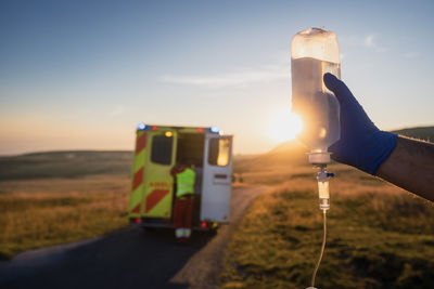 Close-up hand of paramedic holding iv drip against ambulance car of emergency medical service. 