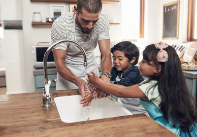 Father washing hands with son and daughter. family learning about hand hygiene and cleaning habits