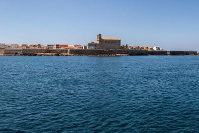 Sea by buildings against clear blue sky