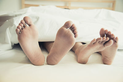 Low section of couple relaxing on bed at home