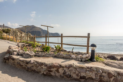 Deck chairs on rocks by sea against sky