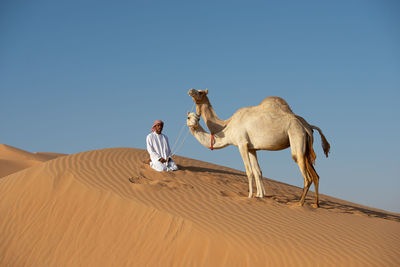 Man on sand dune in desert against clear sky