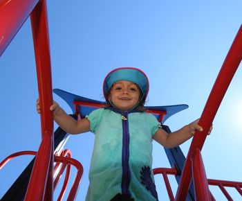 Low angle view of girl on outdoor play equipment against clear sky