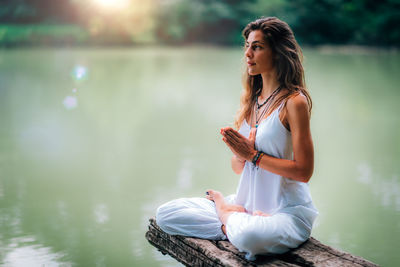 Woman doing yoga while sitting on pier at lake