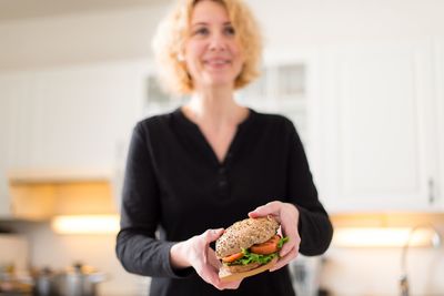 Portrait of smiling mature woman holding burger at home