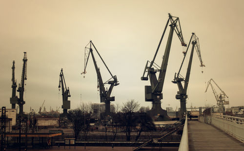 Cranes at harbor against sky in city