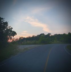 Road by trees against sky during sunset