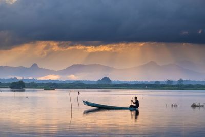 Man on boat in lake against sky during sunset