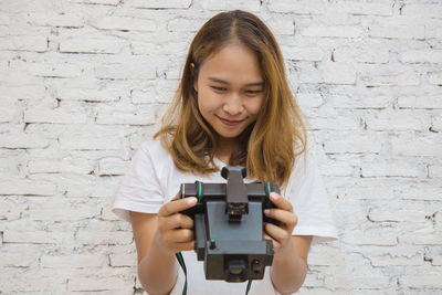 Portrait of girl holding camera against wall