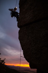 Side view of sportive male alpinist ascending on cliff in mountain terrain at night