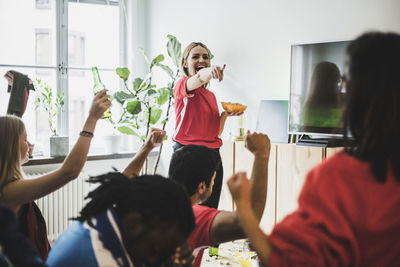 Smiling woman pointing at friends while watching soccer match at home