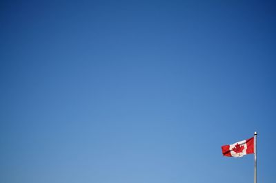 Low angle view of canadian flag against clear blue sky