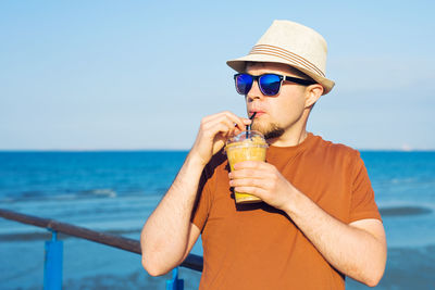 Young man drinking water while standing at beach