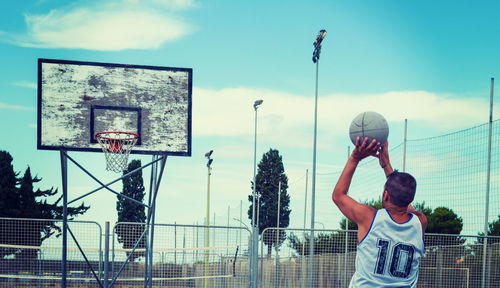 Rear view of man playing basketball hoop against sky