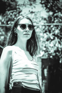 Portrait of young woman wearing sunglasses while standing outdoors during sunny day