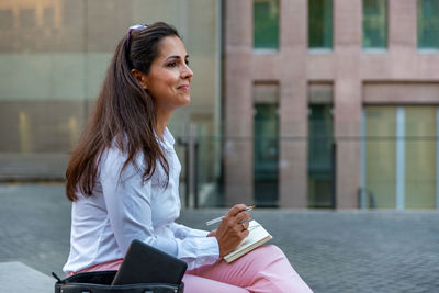 Smiling businesswoman holding diary while sitting outdoors