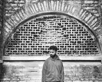 Portrait of young man standing against brick wall