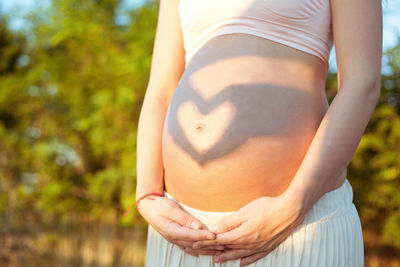 Midsection of pregnant woman standing against trees