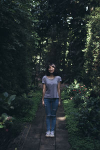 Portrait of smiling young woman standing on footpath in park 