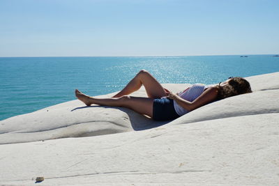 Woman lying down on beach against sky