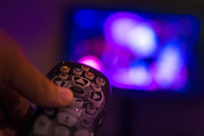 Cropped image of hand holding remote control in front of television set