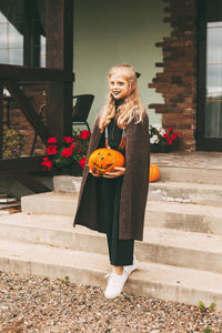 A little blonde girl with makeup for the celebration of halloween holds a pumpkin 