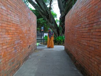 Woman standing on footpath by brick wall