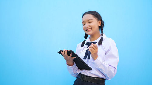 Smiling young woman using mobile phone against blue sky