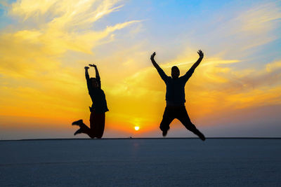 Silhouette people jumping at beach against sky during sunset