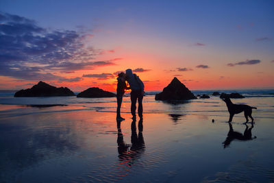 Silhouette people at beach against sky during sunset