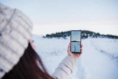 Midsection of person holding mobile phone against sky