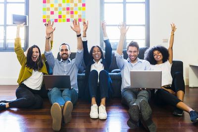 Portrait of happy colleagues cheering sitting on floor with laptops