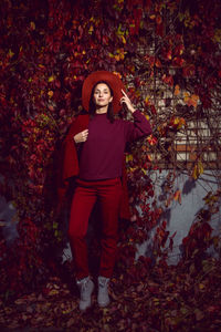 Woman in a red hat and red sweater stands on a background of orange leaves grapes wall autumn