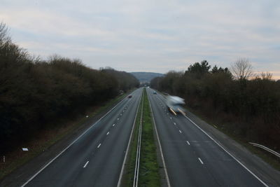 Empty road along trees and against sky