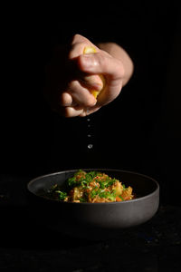 Close-up of hand holding bowl against black background