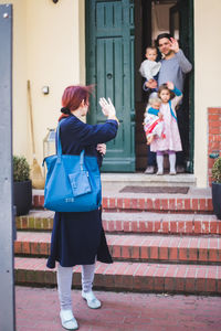 Family at house entrance waving to woman leaving for work