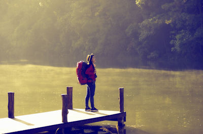 Rear view of woman standing on pier over lake