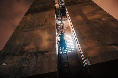 Low angle view of man standing on metallic ladder