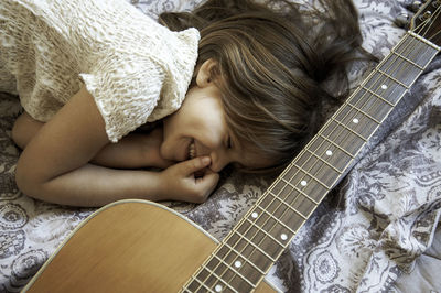 Smiling girl lying on bed by guitar at home