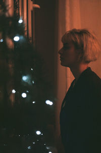Side view of young woman looking at christmas tree at home