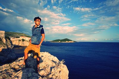 Full length of man standing on rock formation by sea against sky