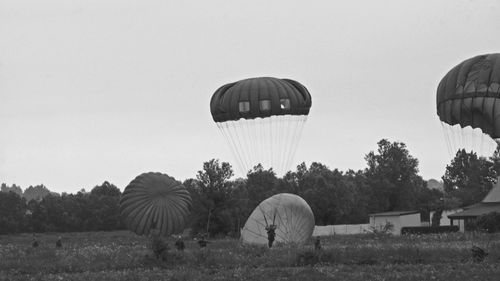 Military soldiers landing on field with parachute against sky